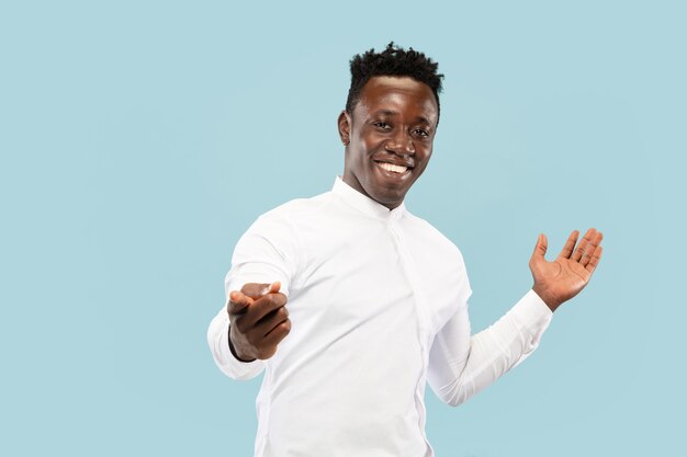 Pointing at you. Young african-american man isolated on blue studio background, facial expression. Beautiful male half-lenght portrait. Concept of human emotions, facial expression.