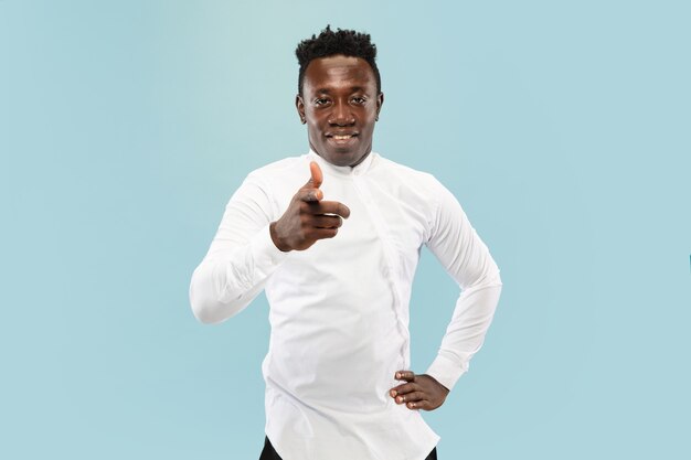 Pointing at you. Young african-american man isolated on blue studio background, facial expression. Beautiful male half-lenght portrait. Concept of human emotions, facial expression.