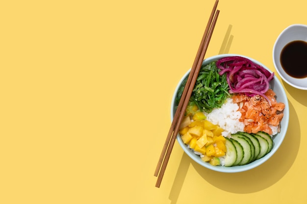 Free photo poke bowl with rice salmoncucumbermangoonionwakame salad poppy seeds ands sunflowers seeds isolated on yellow backgroundxa