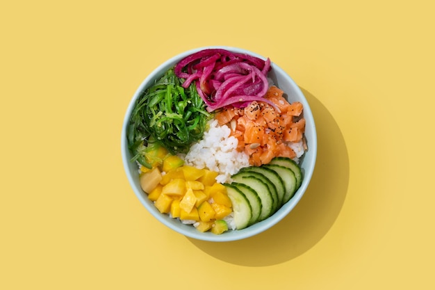 Foto gratuita poke bowl con riso salmonecetriolimangoonionwakame insalata semi di papavero e semi di girasoli isolati su sfondo gialloxa