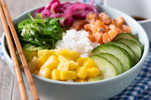 米サーモンきゅうりmangoonionwakame サラダ ケシの実と木製の背景にヒマワリの種とボウルを突く