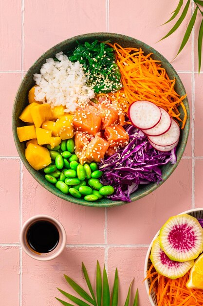 Pokea bowl with fresh salmon rice chuka salad edamame beans carrots and red cabbage Healthy food bowl on pink background Vertical