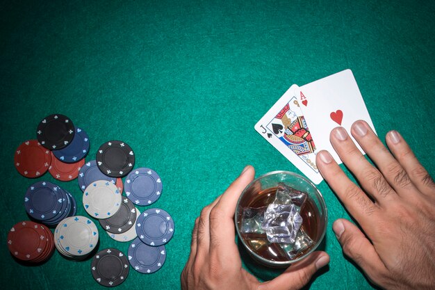 緑のポーカーテーブルにカジノチップを持つジャックとエースカードを見せているポーカープレーヤー