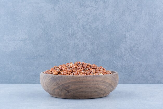 Polished wooden bowl stocked with red beans on marble surface