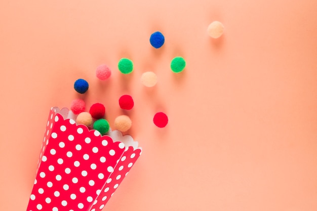 Free photo polka dot cone with spilled colorful yarn balls on peach colored backdrop