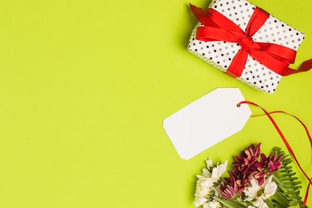 Polka dot wrapped gift box with blank tag and flower bunch on green backdrop