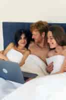 Free photo polyamorous couple at home in bed with laptop