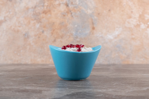 Pomegranate arils on porridge in the plate, on the marble surface