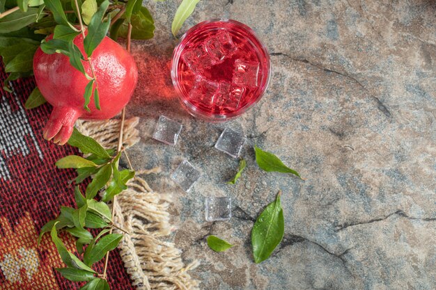 Pomegranate and glass of juice on stone background with leaves