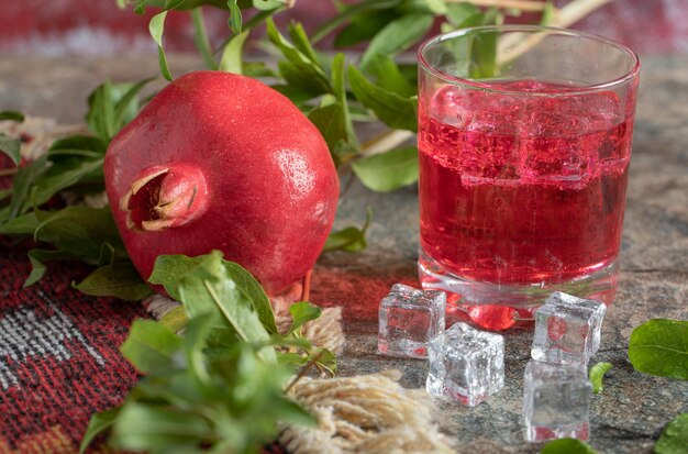 Pomegranate and glass of juice on stone table with leaves