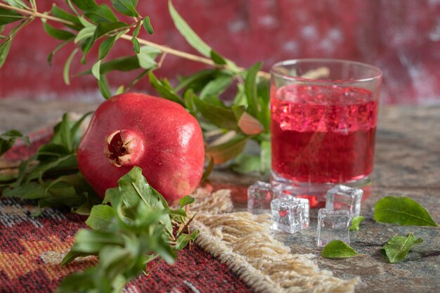 Pomegranate and glass of juice on stone table with leaves