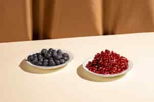 Free photo pomegranate seeds and blueberries on plate over white table near brown curtain