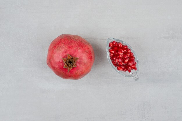 Pomegranate seeds in glass and pomegranate on white surface. 