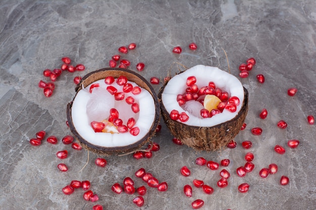 Free photo pomegranate seeds inside coconuts and on surface.