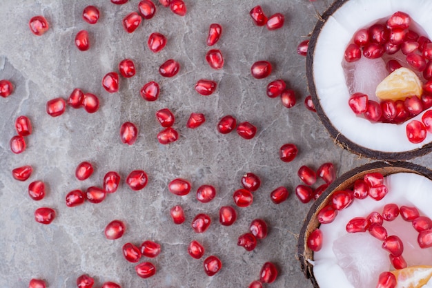 Pomegranate seeds inside coconuts and on surface. 