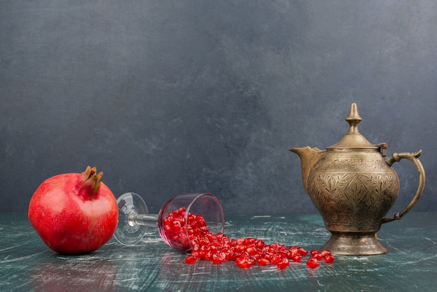 Pomegranate seeds scattered on marble table with teapot.