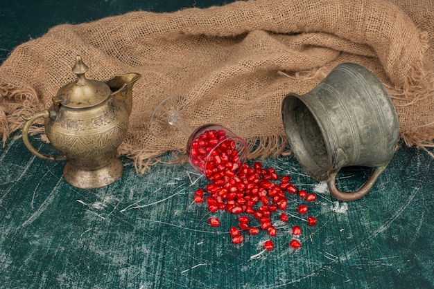 Pomegranate seeds scattered on marble table with vase and teapot.