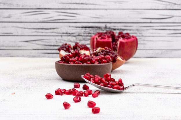 pomegranate seeds in spoon and plate on white table