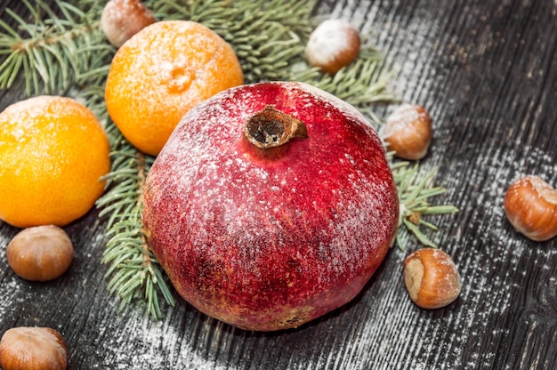 Гранат с мандаринами, орехами и ветвью елки на деревянных фоне. рождественская открытка.