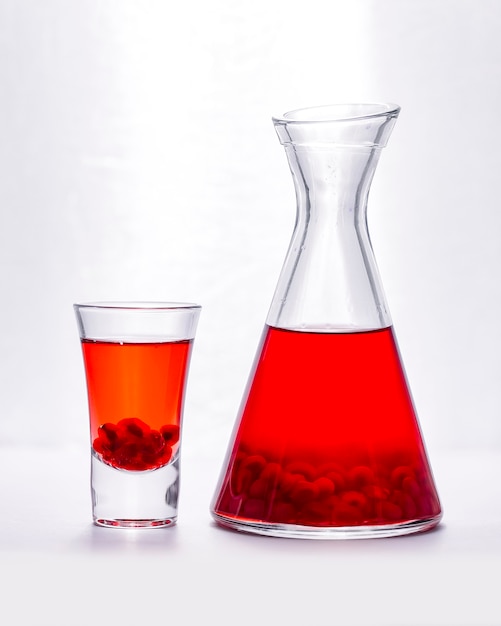 Pomegrante juice in shot glass and jug with seeds inside side view