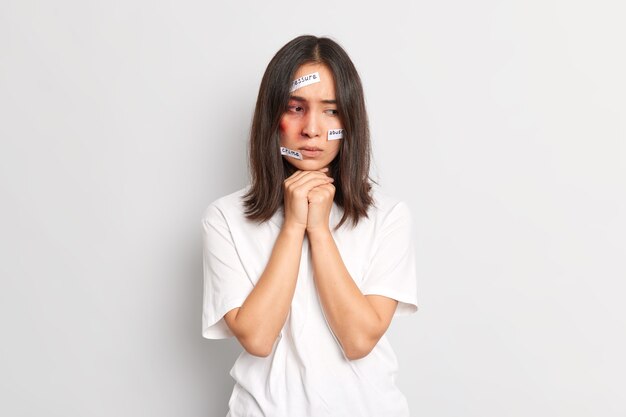 Poor helpless woman looks thoughtfully down has bruises on face becomes victim of killer suffered severe sadistic torture has family problems with husband dressed in whitte t shirt. Depression despair