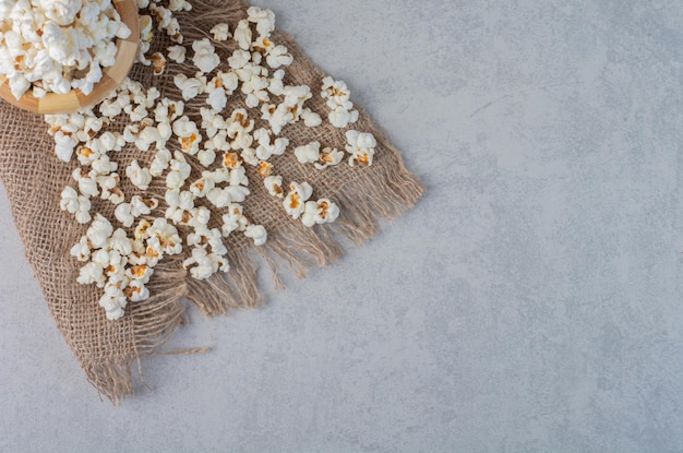 Popcorn in a bowl and scattered on a piece of cloth on marble surface