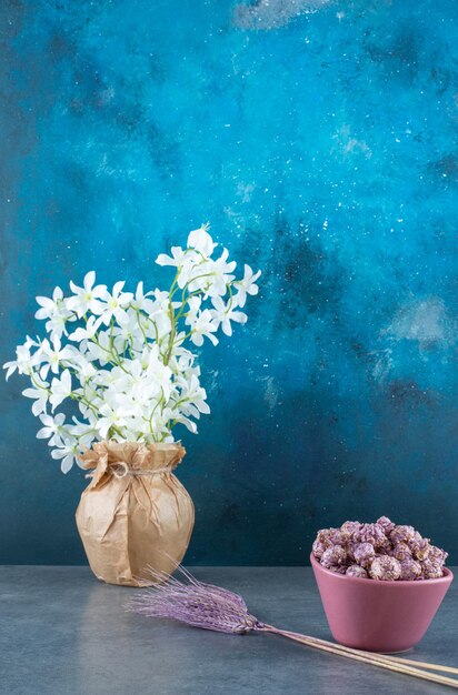 Popcorn candy in a bowl next to purple wheat stalks and white lilies in a wrapped vase on blue