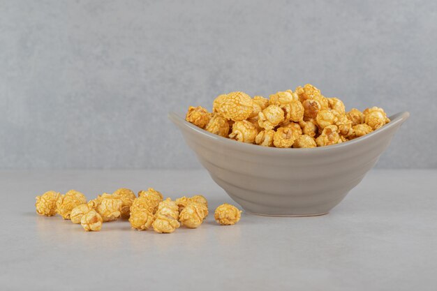 Popcorn coated with caramel inside and next to a small bowl on marble table.