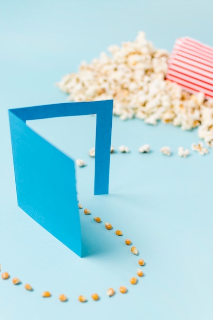 Free photo popcorn seed enter through paper door turning into popcorn against blue background