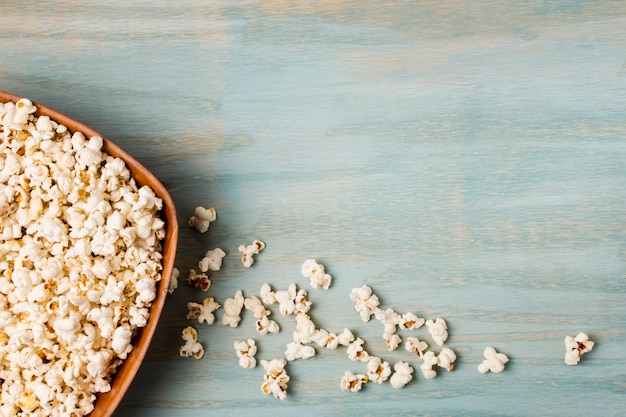 Free photo popcorns spilled from the bowl on blue desk