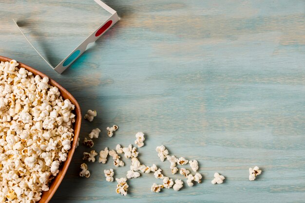 Popcorns spilled from the bowl with blue and red 3d glasses on blue desk