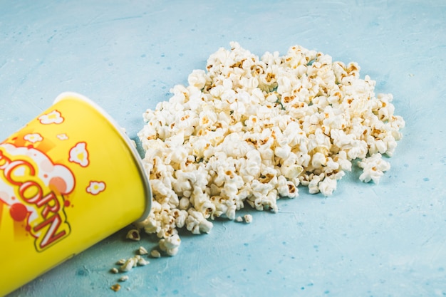 Popcorns spread over the blue table from the yellow container