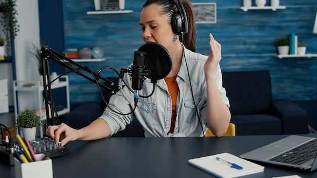 Popular internet streaming influencer putting headphones on and starting to record daily vlog. Social media star sitting at home studio desk while filming podcast video in living room. Studio shoot