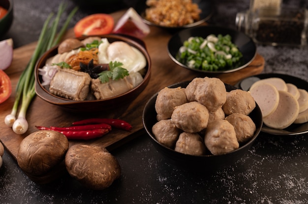 Pork balls in black cups with spring onion, chili, shiitake mushroom, and tomato.