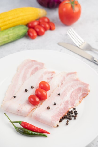 Pork belly sliced on a white plate with pepper seeds and tomatoes.