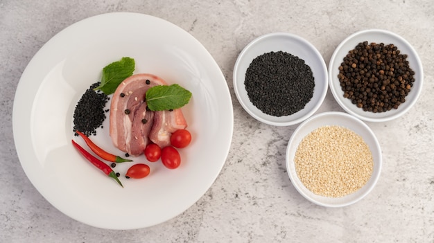 Pork belly sliced Ã¢ÂÂÃ¢ÂÂon a white plate with pepper seeds and tomatoes.