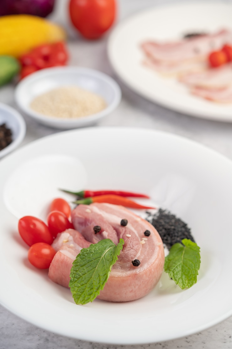 Free Photo pork belly in a white dish with pepper seeds tomatoes and spices.