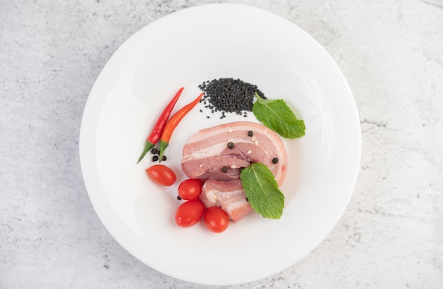 Pork belly in a white dish with pepper seeds Tomatoes and spices.