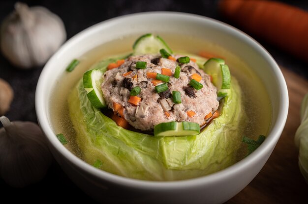 Pork cabbage soup with carrots, chopped green onions, cucumber in a wooden plate on a wooden plate