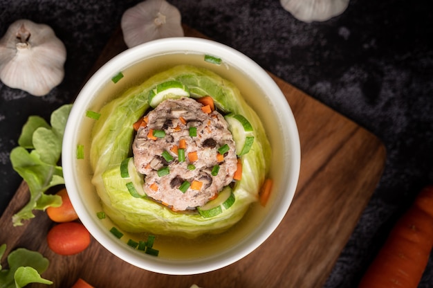 Pork cabbage soup with carrots, chopped green onions, cucumber in a wooden plate on a wooden plate