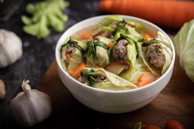 Pork cabbage soup with carrots, chopped green onions, cucumber in a wooden plate on a wooden plate