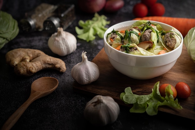 Pork cabbage soup with carrots, chopped green onions, cucumber in a wooden plate on a wooden plate