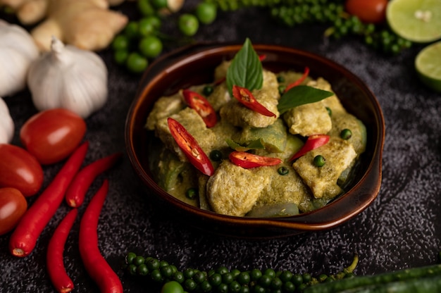 Pork green curry in a brown bowl with spices on a black cement background