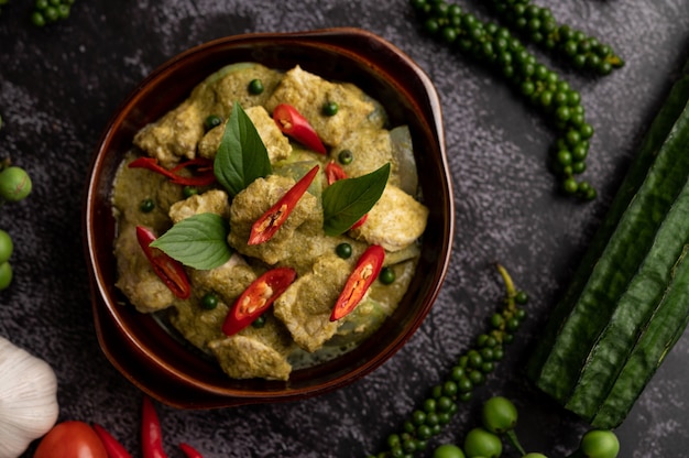 Pork green curry in a brown bowl with spices on a black cement background