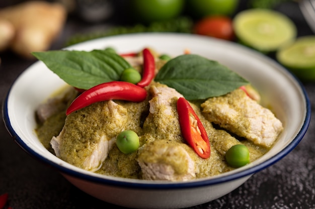 Pork green curry in a white bowl with spices on a black cement background