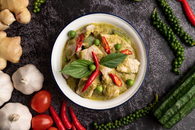 Pork green curry in a white bowl with spices on a black cement background