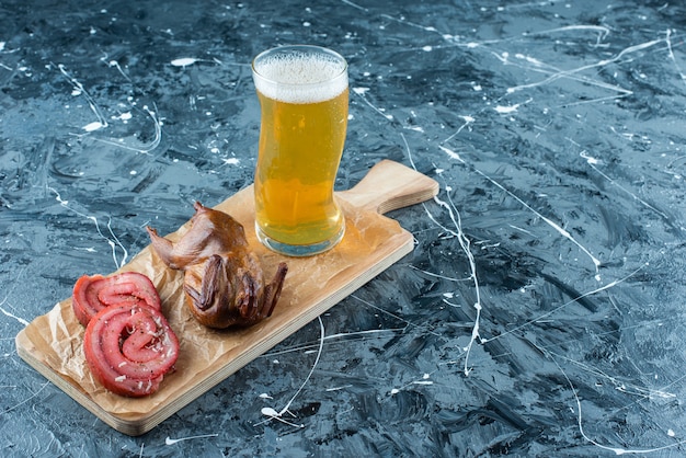Сало свинины, гриль и пиво на разделочной доске, на синем столе.