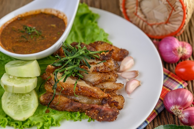 Pork neck grilled on a white plate wiht red onion, tomato, and chili on the wooden table.