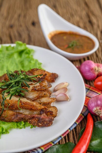 Pork neck grilled on a white plate wiht red onion, tomato, and chili on the wooden table.