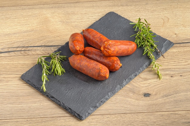 Pork sausages and rosemary leaves on a gray textured board on a wooden table